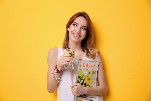 Mooie jonge vrouw met limonade en tijdschrift op kleur