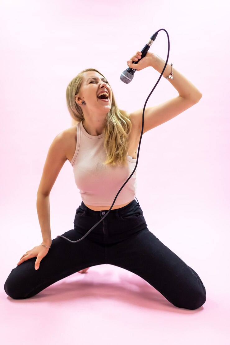 Foto mooie jonge vrouw met microfoon zingen op roze achtergrond