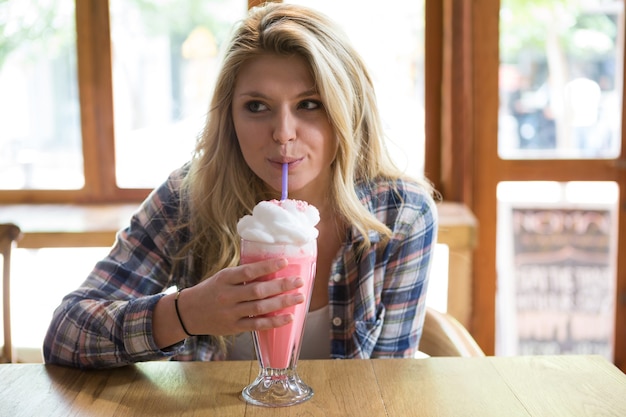 Mooie jonge vrouw met milkshake aan tafel in de coffeeshop