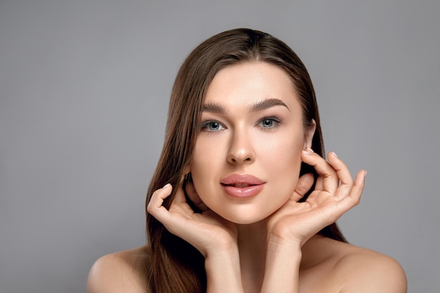 Mooie jonge vrouw met natuurlijke make-up en schone, frisse huid raakt het eigen gezicht aan Gezichtsbehandeling