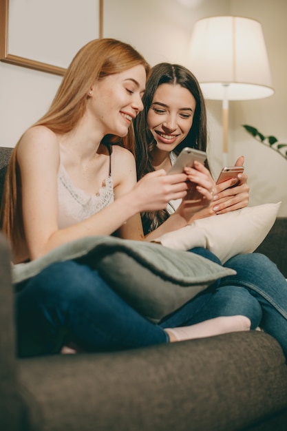 Mooie jonge vrouw met rood haar en sproeten iets op haar smartphonescherm tonen aan haar vriend zittend op de bank lachen.