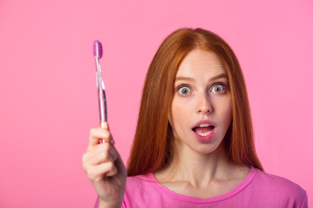 mooie jonge vrouw met rood haar op een roze achtergrond met een tandenborstel