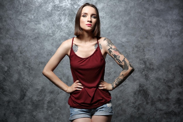 Mooie jonge vrouw met tatoeage die zich voordeed op grijze achtergrond
