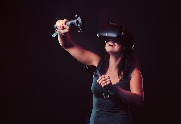 Mooie jonge vrouw met virtual reality-headset en joysticks die videogames spelen. geïsoleerd op donkere achtergrond.