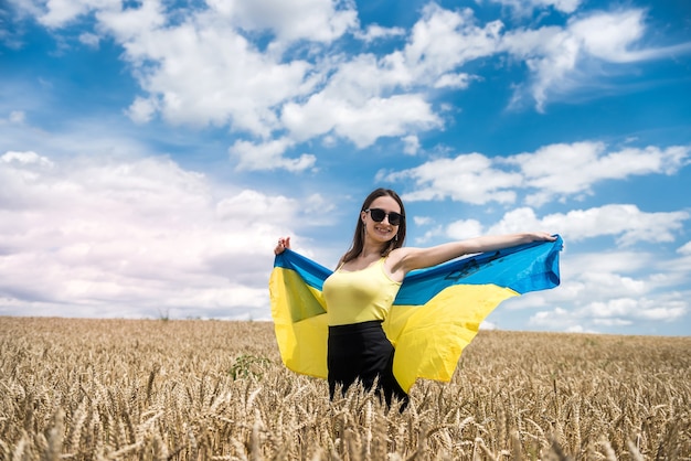 Mooie jonge vrouw met vlag van Oekraïne in de zomertijd van het tarweveld