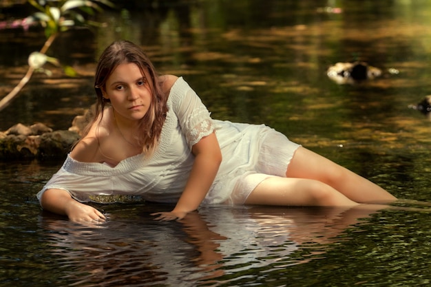 Mooie jonge vrouw met witte jurk in de buurt van stroom van water.