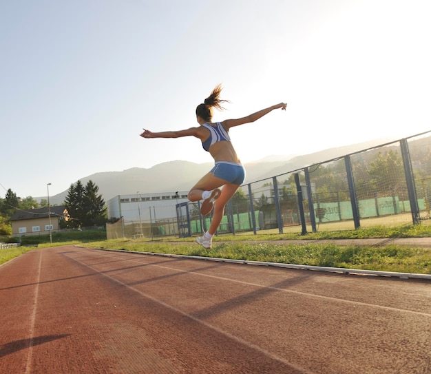 mooie jonge vrouw oefent joggen en rennen op atletiekbaan op stadion bij zonsopgang