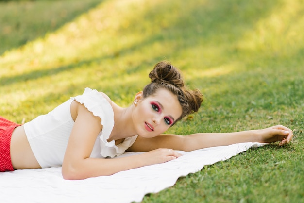 mooie jonge vrouw of meisje met lichte make-up ligt op een deken op het gazon in de zomer op een picknick