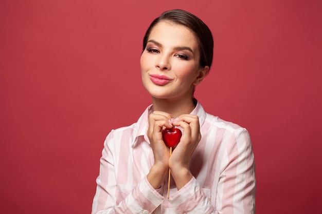 Mooie jonge vrouw omhelst in de vorm van een hart rood hart en glimlacht op rode achtergrond