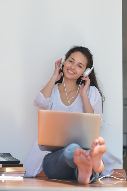 mooie jonge vrouw ontspannen en werken op laptopcomputer terwijl u naar muziek luistert op een koptelefoon en thuis een boek leest