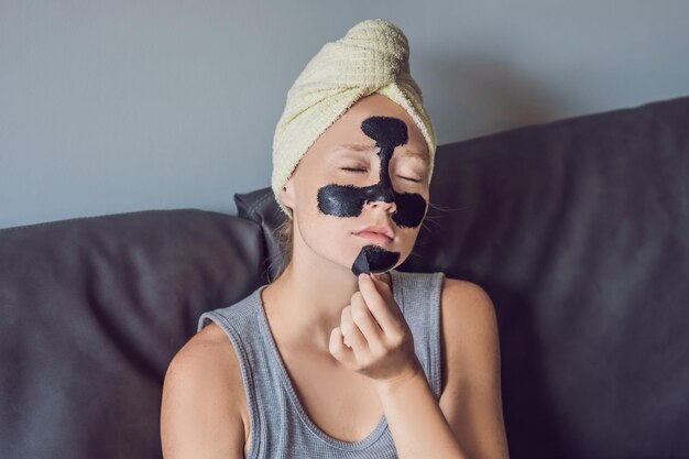 Mooie jonge vrouw ontspannen met gezichtsmasker thuis. Gelukkige vrolijke vrouw die zwart masker op gezicht toepast