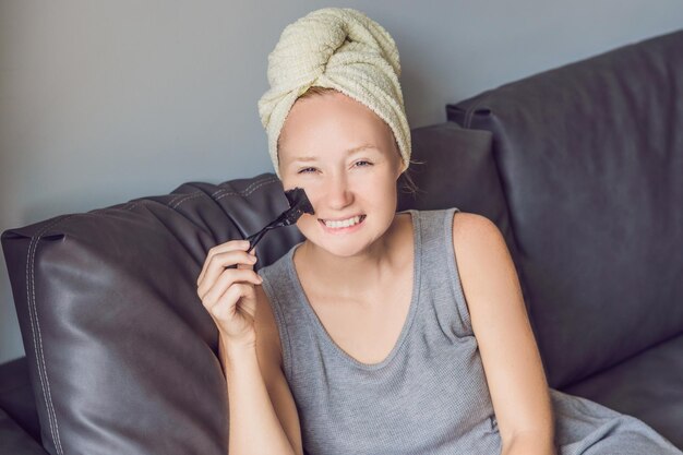 Mooie jonge vrouw ontspannen met gezichtsmasker thuis. Gelukkige vrolijke vrouw die zwart masker op gezicht toepast