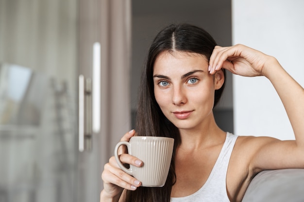 Mooie jonge vrouw ontspannen op een bank thuis, kopje houden