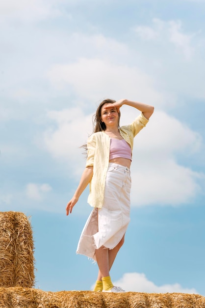 Mooie jonge vrouw poseert voor foto staand in hooi Blauwe lucht Zomerdag Verticaal frame