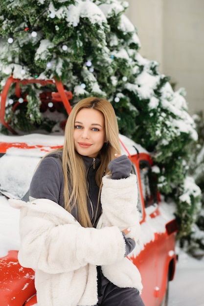 Mooie jonge vrouw poseren in de buurt van een retro rode auto in de winter