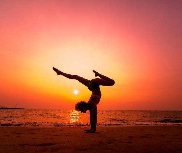 Mooie jonge vrouw praktische yoga op het strand. Ochtendtraining. zonsopkomst