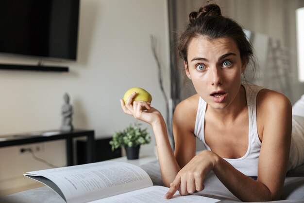 Mooie jonge vrouw realxing op een bank thuis, lezen, groene appel eten