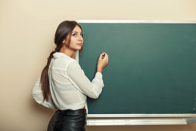 Mooie jonge vrouw schrijft krijt op het bord