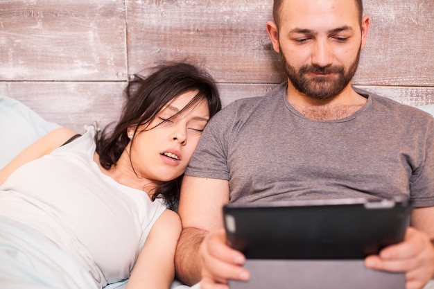 Mooie jonge vrouw slapen naast haar man. Man usint tabletcomputer.