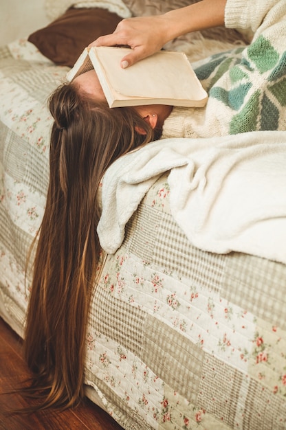 Mooie jonge vrouw slapen op bed met boek dat haar gezicht bedekt, omdat het lezen van boek met het voorbereiden van examen van de universiteit, vrouw slaperig met moe zodat vrije tijd, ontspanning en onderwijs concept.