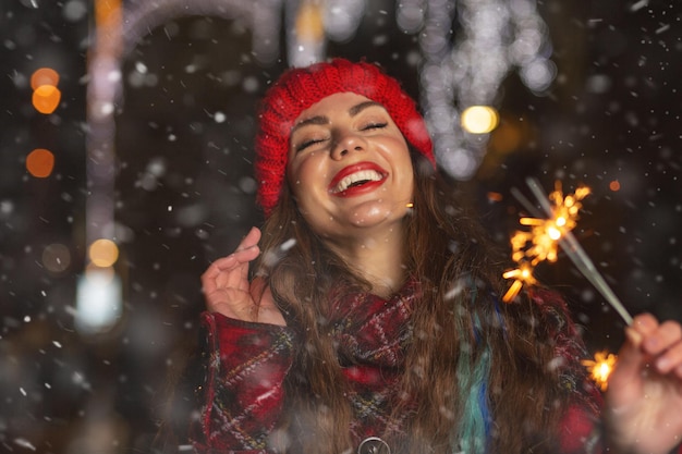 Mooie jonge vrouw spelen met sterretjes op straat tijdens sneeuwval