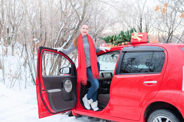 Mooie jonge vrouw staat in een rode auto versierd voor Kerstmis in het winterbos tijdens Xmas