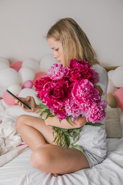 mooie jonge vrouw thuis in de slaapkamer in bed met bloemen neemt een selfie via de mobiele telefoon