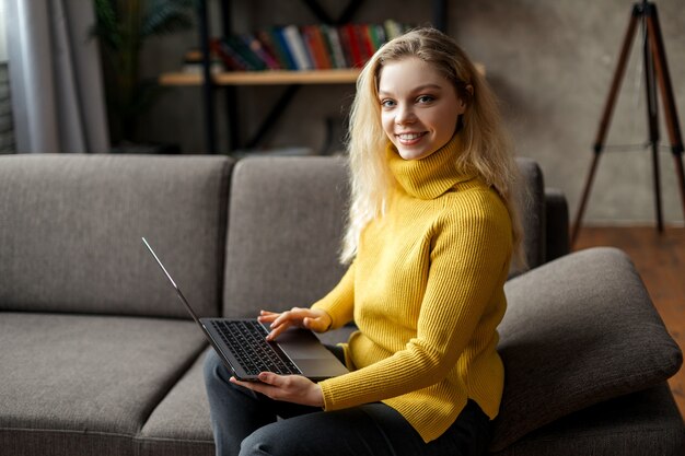 Mooie jonge vrouw thuis werken op een laptop zittend op de bank in de woonkamer. Hoge kwaliteit foto