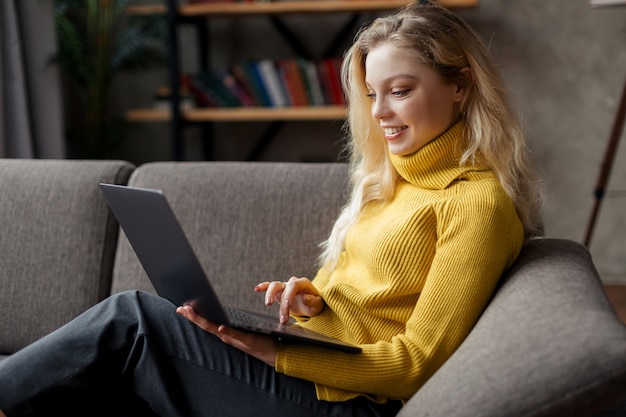 Mooie jonge vrouw thuis werken op een laptop zittend op de bank in de woonkamer