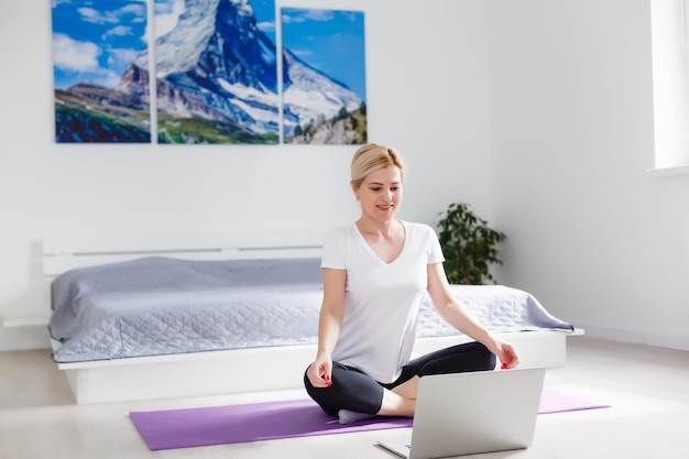 Foto mooie jonge vrouw training online thuis op laptopcomputer, kopieer ruimte. volledig portret. yoga, pilates, sporten sporten