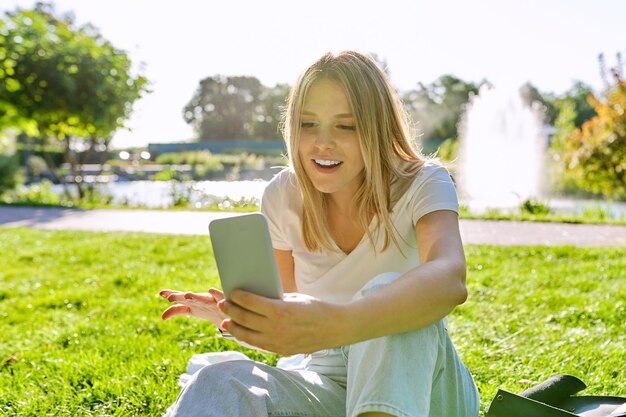 Mooie jonge vrouw videobellen op smartphone, vrouw zittend op gras in park, rust online communicatie met vrienden, student praten, blogger bloggen blog vlog