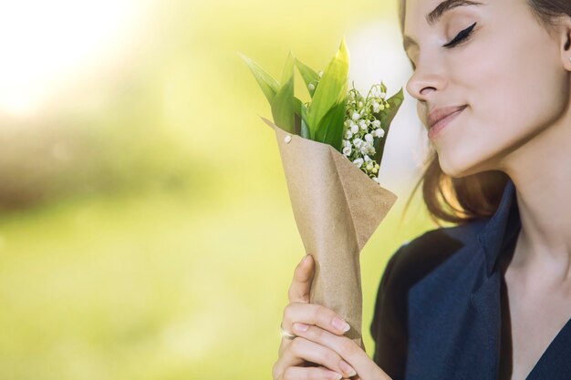 Mooie jonge vrouw wandelen in het park met een boeket van lelietje-van-dalen in de handen van het portret