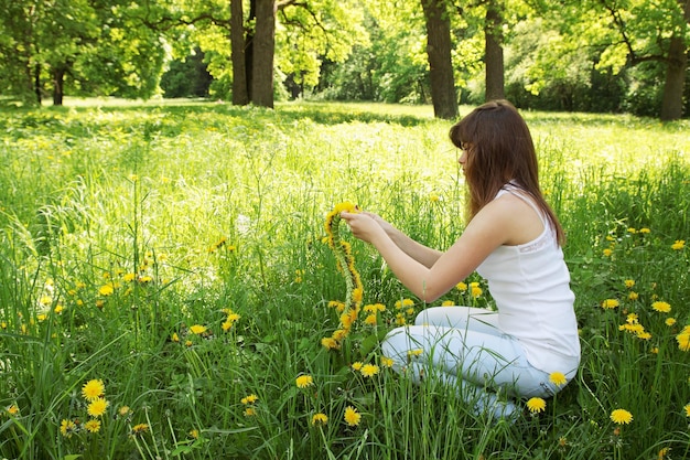 Mooie jonge vrouw weeft een krans van paardebloemen