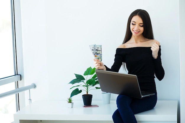 Mooie jonge vrouw werkt op de computer, gekleed in zwarte jas en spijkerbroek