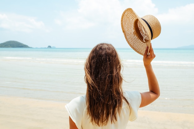 Mooie jonge vrouw werpt haar hoed op een zonnig strand