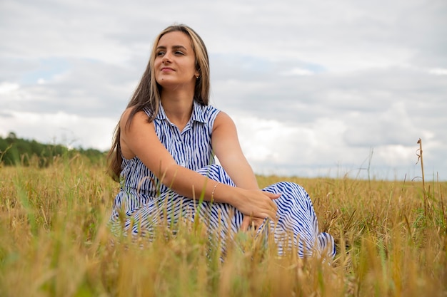 mooie jonge vrouw zit in een weiland in bloemen op een zonnige zomerdag en glimlacht.