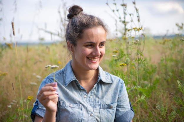 Mooie jonge vrouw zit in een weiland in bloemen op een zonnige zomerdag en glimlacht