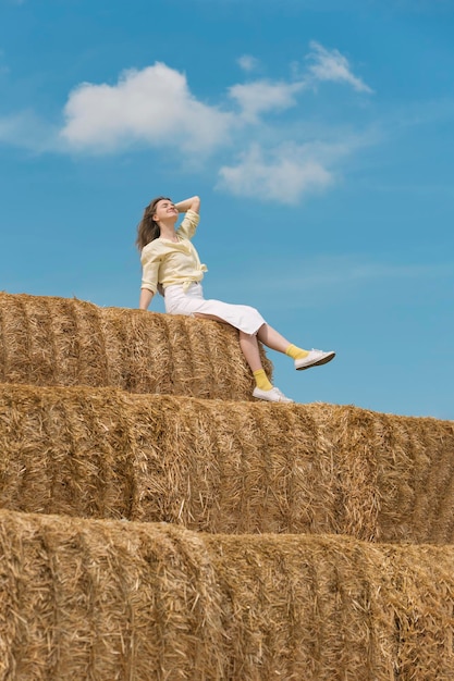 Mooie jonge vrouw zit op een enorme hooiberg Lokaal toerisme Zonnige dag op de boerderij Vakantie op het platteland