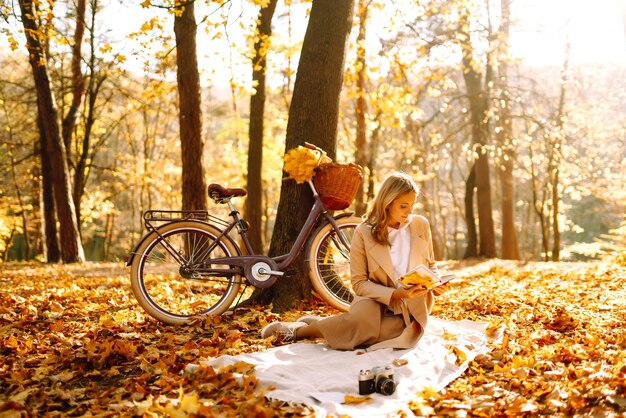 Mooie jonge vrouw zit op een gevallen herfstblad in een park en leest een boek Relaxation