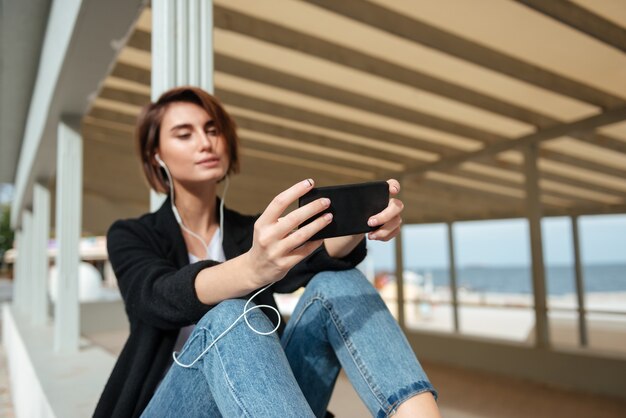 Mooie jonge vrouw zitten en luisteren naar muziek van de mobiele telefoon in de veranda op het strand