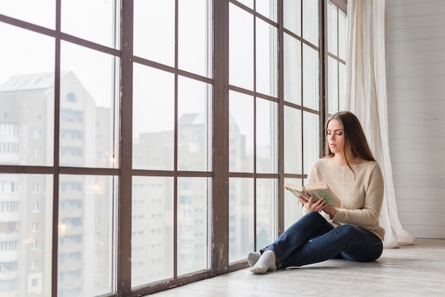 Foto mooie jonge vrouw zitten in de buurt van het leesboek glasvenster