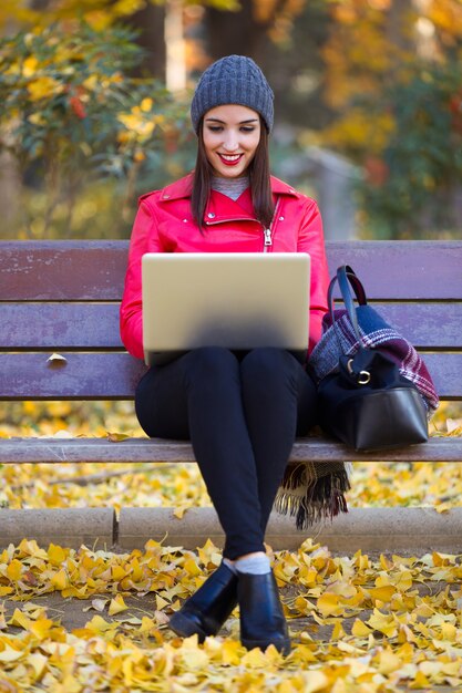 Mooie jonge vrouw zitten in een bankje en het gebruik van haar laptop in de herfst.