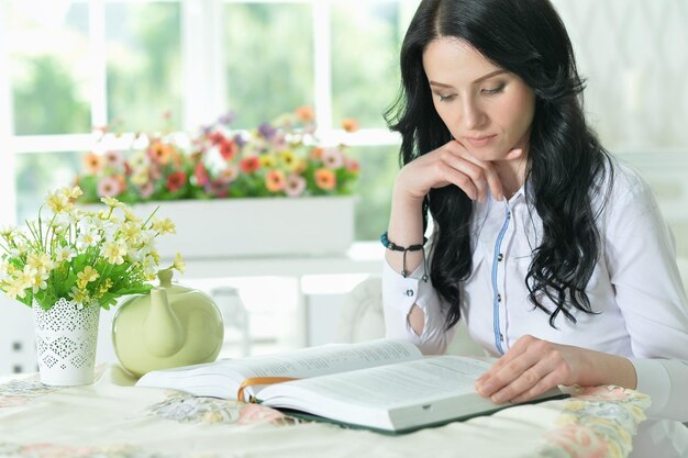 Mooie jonge vrouw zittend aan tafel met geopend boek