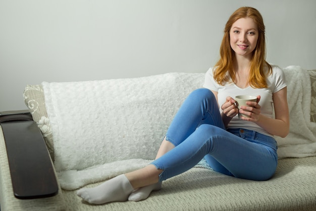 mooie jonge vrouw zittend op de bank met een mok drankje