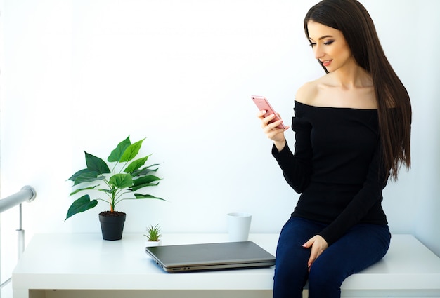 Mooie jonge vrouw zittend op een bureau met een map en een telefoon.