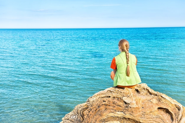 Foto mooie jonge vrouw zittend op een grote rots en kijkend naar de blauwe zee