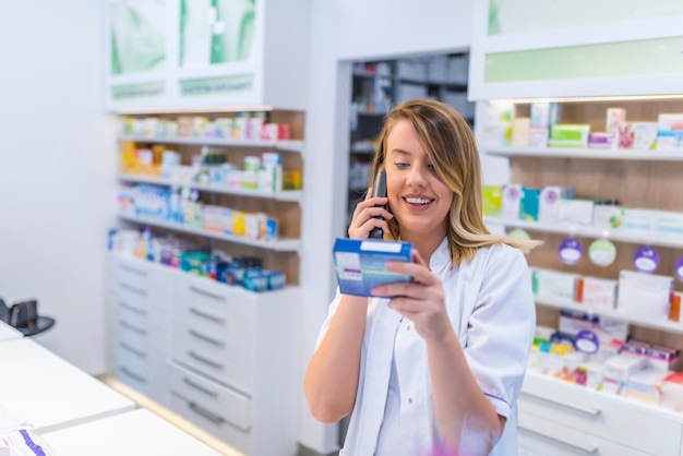 Mooie jonge vrouwelijke apotheker die op de telefoon spreekt