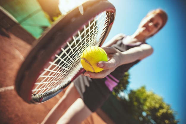 Mooie jonge vrouwelijke tennisspeelster die zich voorbereidt om te dienen op tenniswedstrijd.