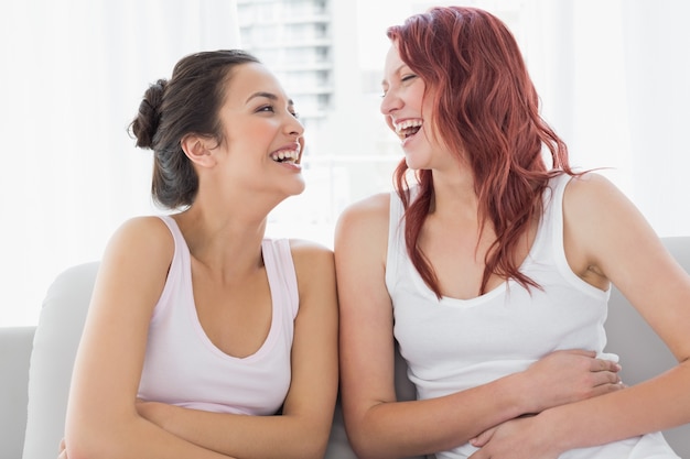 Mooie jonge vrouwelijke vrienden die in woonkamer lachen