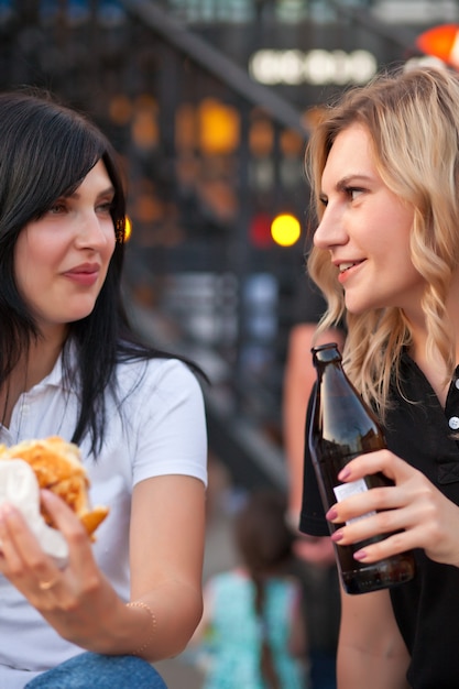 Mooie jonge vrouwen die hamburger buiten op straat eten.